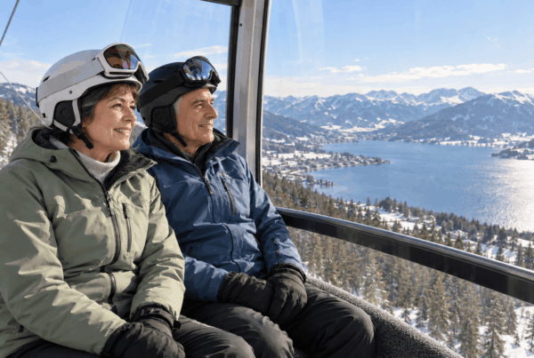 Skifahren im Alter: Älteres Paar genießt eine Gondelfahrt mit Blick auf einen See und verschneite Berge.